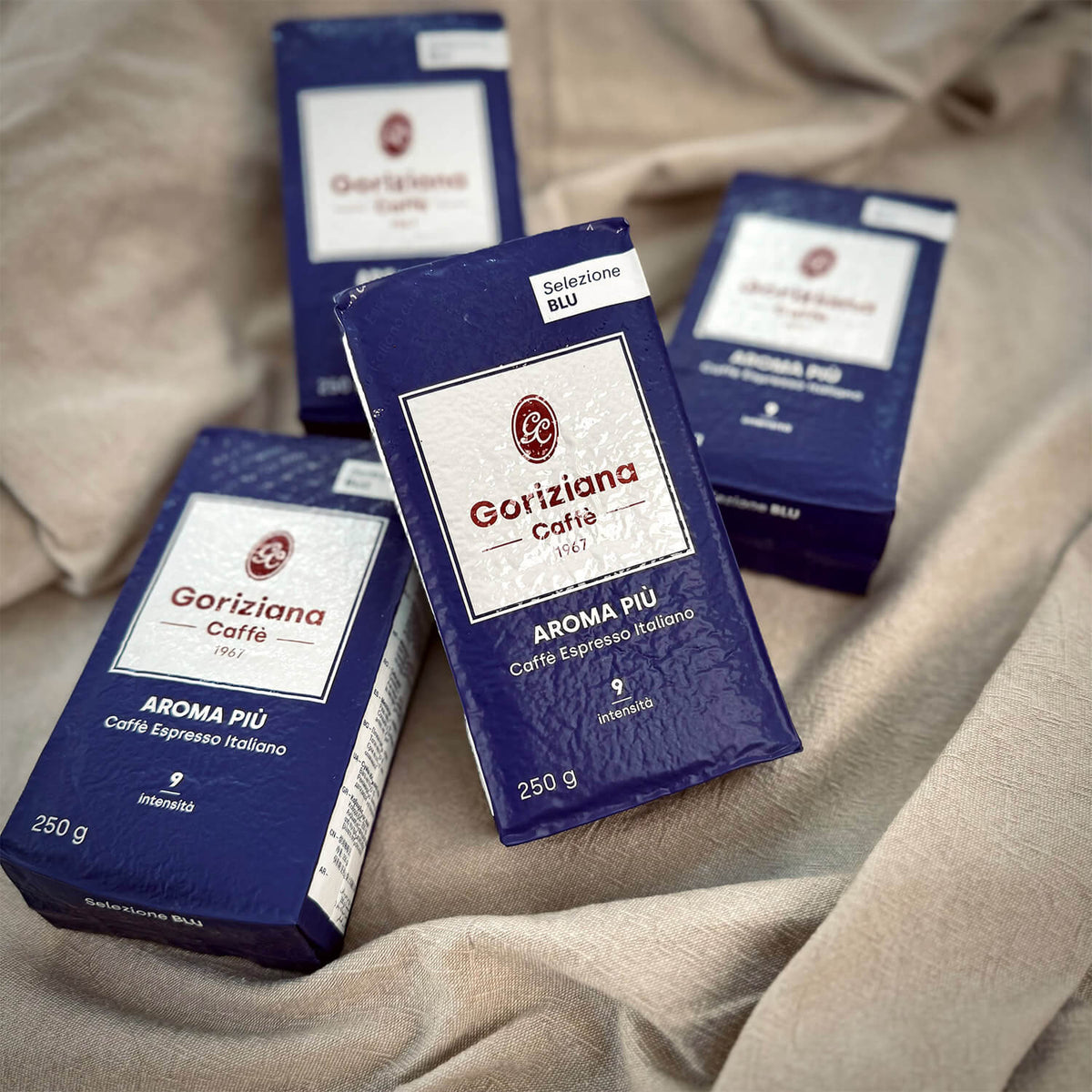 Vier Packungen Torrefazione Goriziana Espresso gemahlen BLU Aroma Piu Kaffee werden auf einem beigen Stoffhintergrund präsentiert.