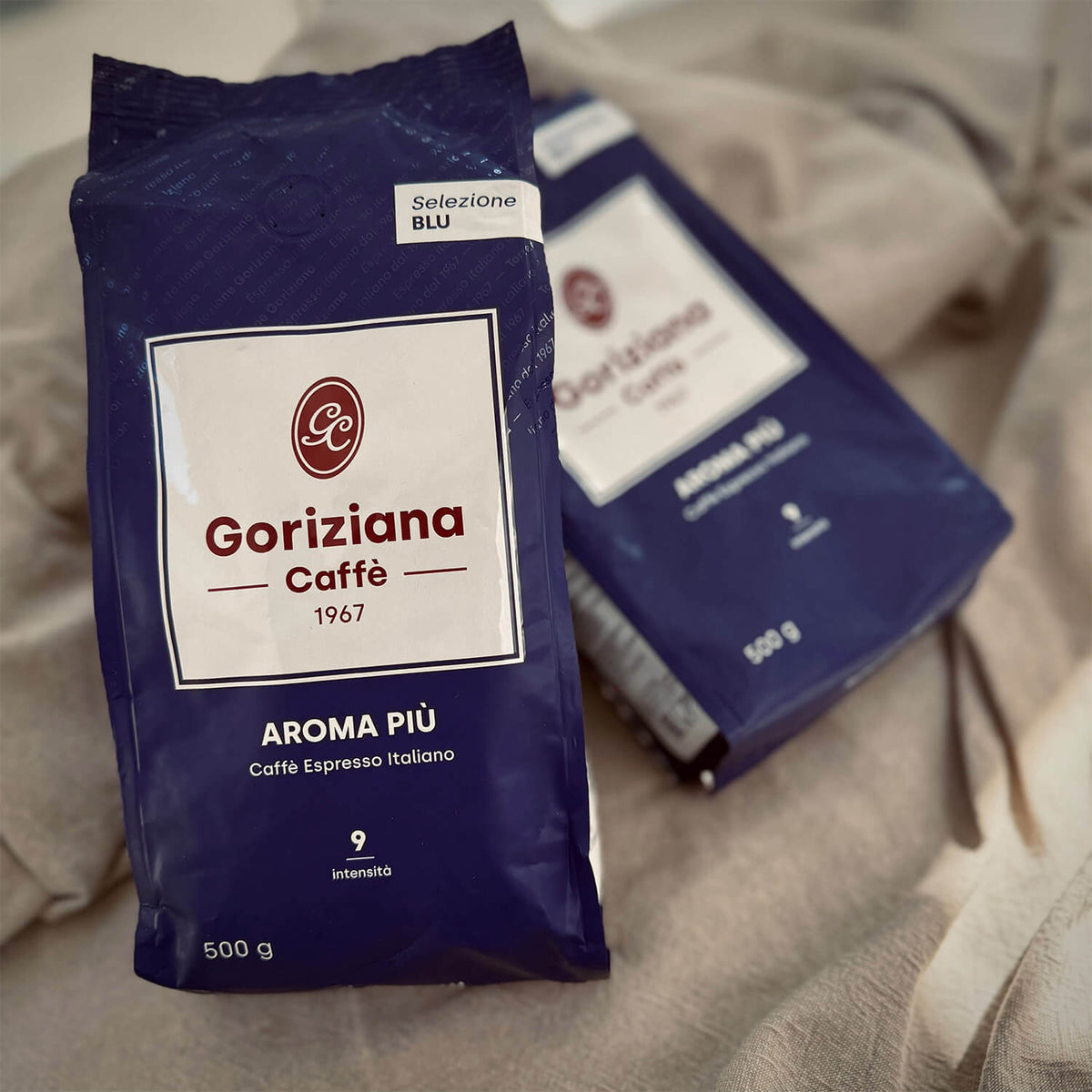 Zwei blaue Beutel Torrefazione Goriziana Espresso Bohnen BLU Aroma Piu (2 x 500g) liegen auf einer beigen Stoffunterlage.