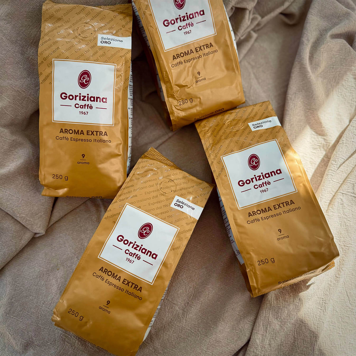 Vier Packungen Torrefazione Goriziana Espresso Bohnen ORO Extra Gold (4 x 250g) auf einer beigen Stoffunterlage.