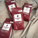Vier Packungen Torrefazione Goriziana Espresso Bohnen ROSSA Aroma Classico, 4 x 250 g, sind auf einem hellbeigen Stoffgrund platziert.