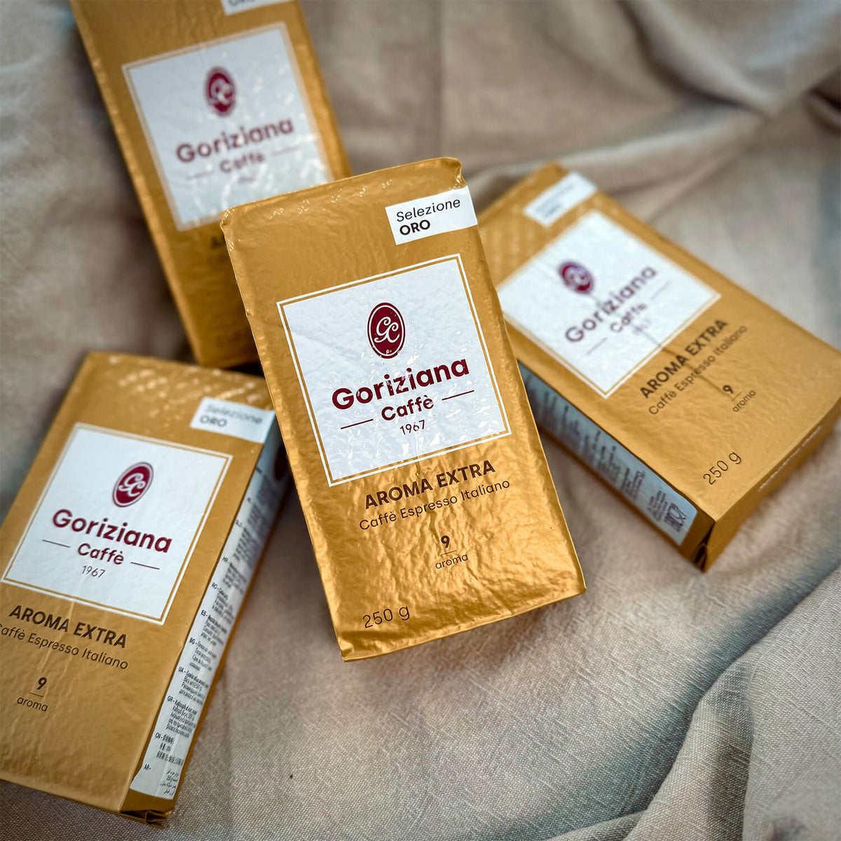 Vier Packungen Torrefazione Goriziana Espresso gemahlen ORO Extra Gold (4 x 250 g) sind auf einer beigen Stoffunterlage angeordnet.