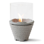Das Schmelzfeuer® Indoor Granicium® mit Windglasaufsatz von Denk by Denk Keramik ist eine kompakte Tischfeuerstelle mit einem Sockel aus Stein, einem Windschutz aus Glas und einer sichtbaren Flamme.