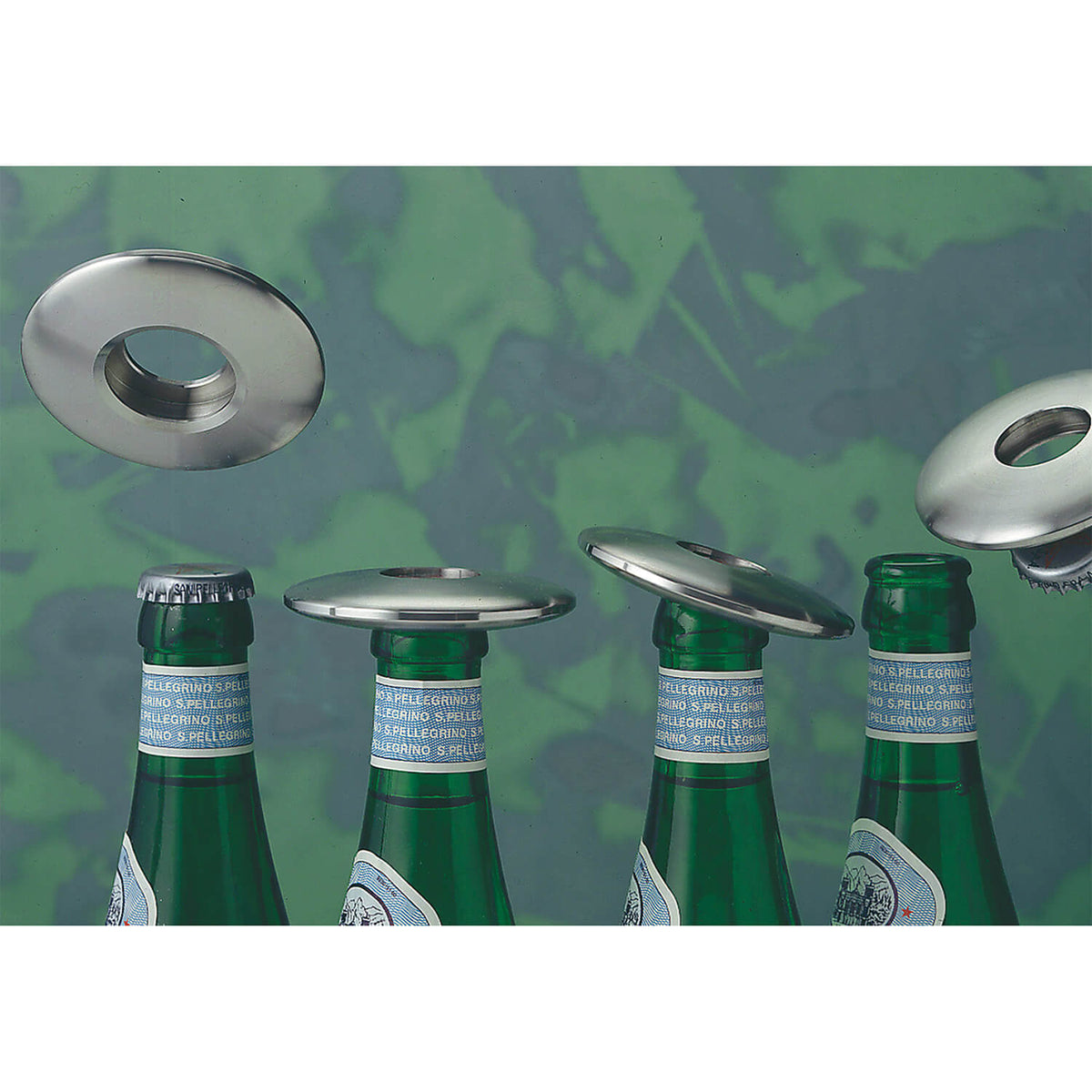 Vier Odin GmbH Flaschenöffner Disc aus Aluminium Ø 7 cm schweben über vier Glasflaschenverschlüssen vor einem grün gesprenkelten Hintergrund.