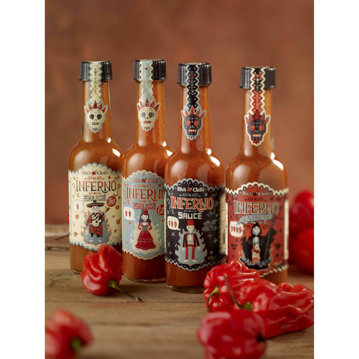 Mics Chili-Saucen-Bundle: Vier farbenfrohe Flaschen (660g, 6.000-100.000 Scoville) liegen auf Holz und sind von roten Chilischoten umgeben.
