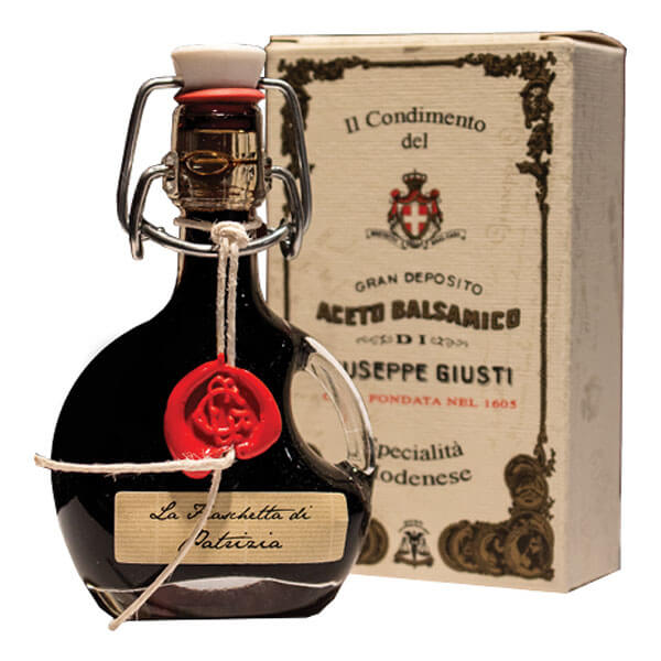 Eine runde 40-ml-Flasche Giuseppe Giusti Il condimento Fiaschetta di Patrizia Balsamico-Essig, die mit Wachs und Schnur versiegelt ist, wird vor ihrer Giuseppe Giusti-Verpackung im Vintage-Stil präsentiert.