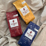 Drei Torrefazione Goriziana Espresso Bohnen Probierpakete (3 x 250g) sind auf einem beigen Stoffhintergrund angeordnet.